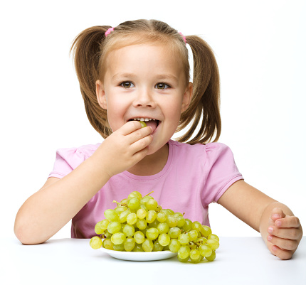 Little girl is eating grapes, isolated over white