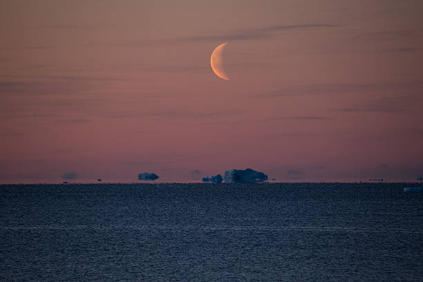 istock Orange sky with Half-moon over Icebergs floating near horizon 623882634