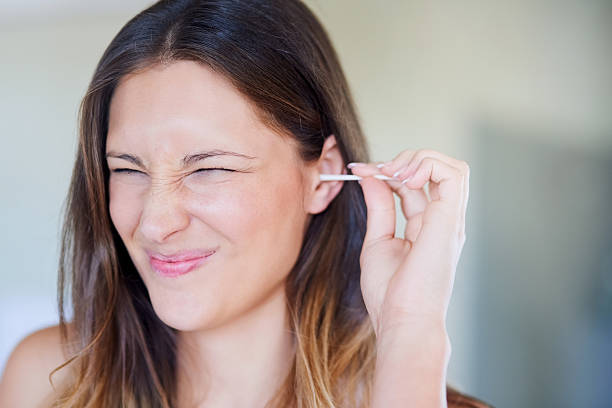 That tickles! Shot of young woman pulling a funny face while cleaning her ear with an earbud at home hair length stock pictures, royalty-free photos & images