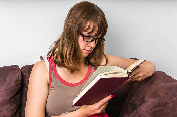 istock Young woman reading a book and sitting on the sofa 623888048