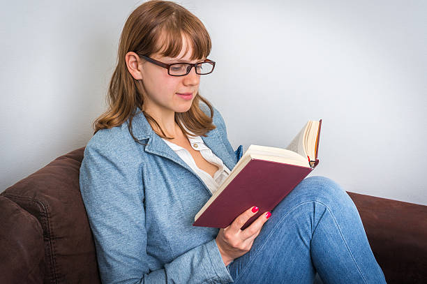 istock Young woman reading a book and sitting on the sofa 623888568