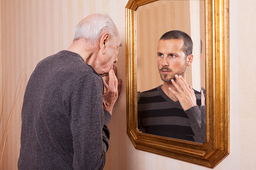 Elder man looking at an younger himself in the mirror