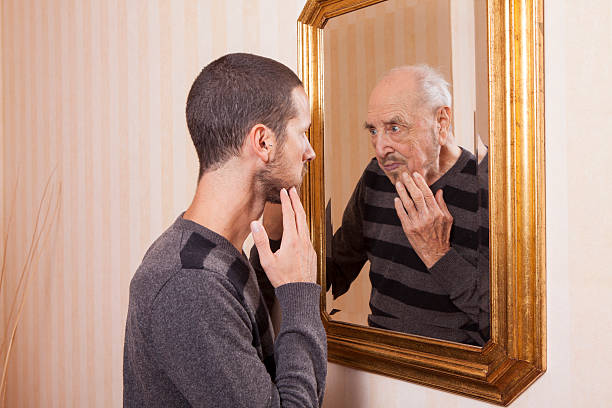 young man looking at an older himself in the mirror - look into the mirror imagens e fotografias de stock