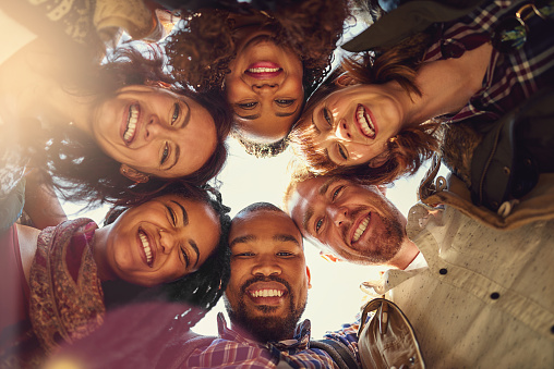 Low angle view photo of a smiling multi-ethnic group join and raising hands