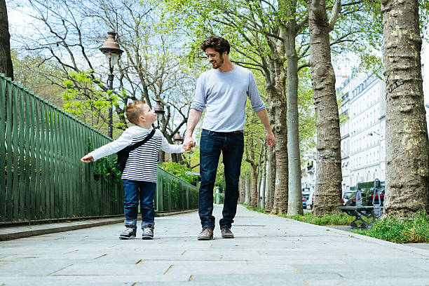 Father And Son Walking Through The Park, Going To School Happy father and son walking through a park. He is taking his son to school before to go to work. way to school stock pictures, royalty-free photos & images
