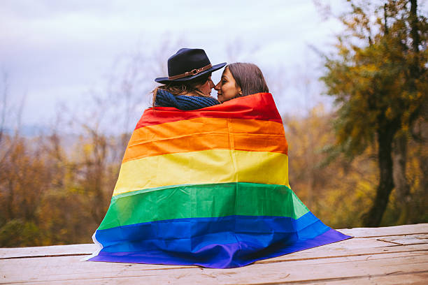 虹の旗の後ろにキスレズビアンの女性 - homosexual gay man symbol homosexual couple ストックフォトと画像
