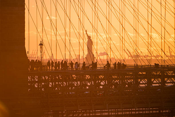 The sun sets behind the Brooklyn Bridge as with a view of the Statue of Liberty.