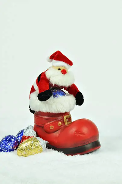 Santa Claus with sweets inside a red boot with white fur trimming on snow background, close up, space for text, vertical