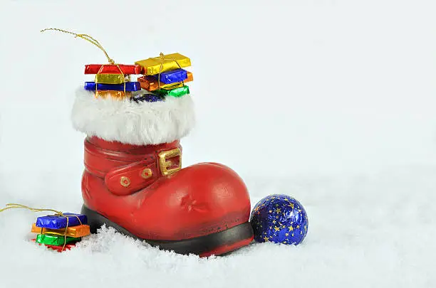 red boot  with white fur trimming, filled  with sweets on snow background, close up, space for text, horizontal
