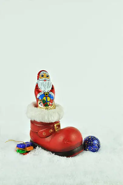 red boot  with white fur trimming, filled  with sweets  and chocolate santa claus on snow background, close up, space for text, vertical