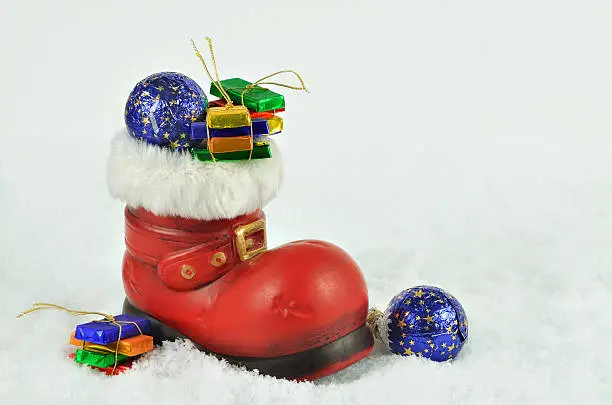 red boot  with white fur trimming, filled  with sweets on snow background, close up, space for text, horizontal