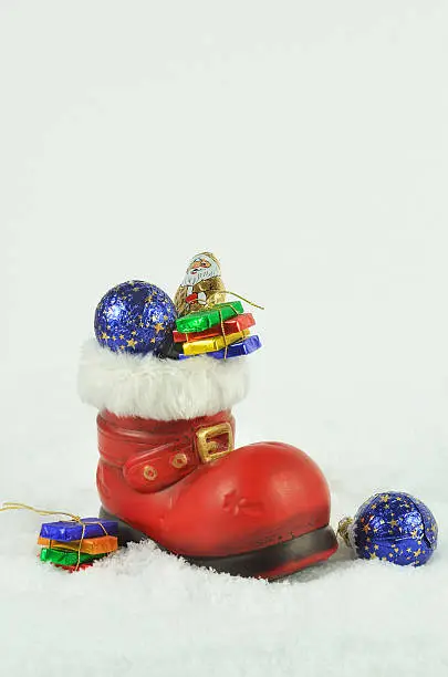 red boot  with white fur trimming, filled  with sweets on snow background, close up, space for text, vertical