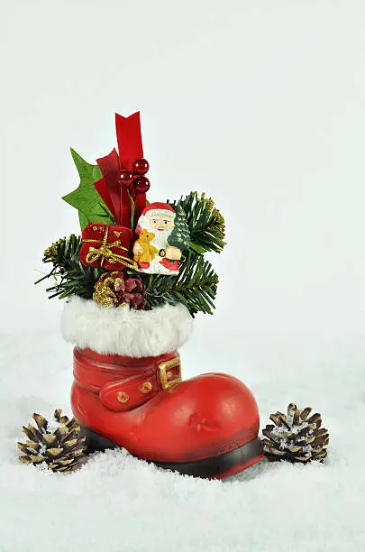 red boot  with white fur trimming, filled  with sweets, fir sprigs  and santa claus on snow background with pine cones, close up, space for text, vertical