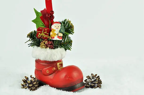 red boot  with white fur trimming, filled  with sweets, fir sprigs and santa claus  on snow background with pine cones, close up, space for text, horizontal