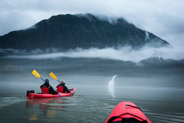 Two paddlers explore Mendenhall Lake in Alaska Alaska, USA - August 11, 2016: Man and woman couple paddles a red kayak across misty Mendenhall Lake toward a waterfall on an adventurous journey on a cloudy overcast day in Juneau. juneau stock pictures, royalty-free photos & images