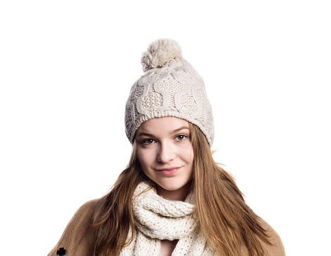 Teenage girl in brown winter coat and woolen scarf and hat, young woman, studio shot on white background. Isolated.