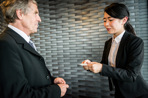 Happy senior Caucasian businessman and a young Japanese businesswoman/entrepreneur are exchanging their business cards, Kyoto, Japan, Asia. At the moment the young lady is giving her card. Office interior, copy space. Nikon D800, full frame, XXXL. iStocklypse Kyoto 2016.