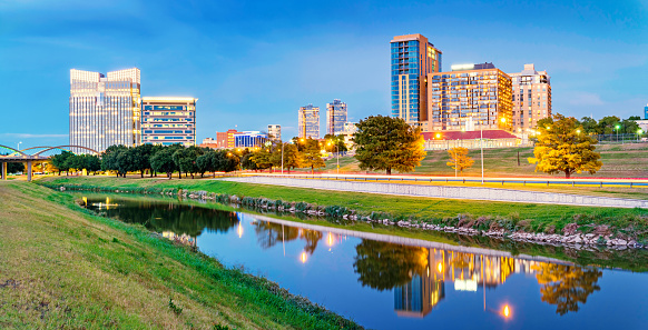 Panoramic photo of the skyline of Fort Worth with apartments and office buildings reflecting in the Clear Fork Trinity River at Trinity Park, in downtown Fort Worth,Texas, USA.