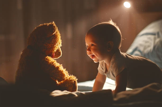 Happy baby laughing with teddy bear in bed Happy baby laughing with teddy bear in bed in the dark teddy bear night light stock pictures, royalty-free photos & images