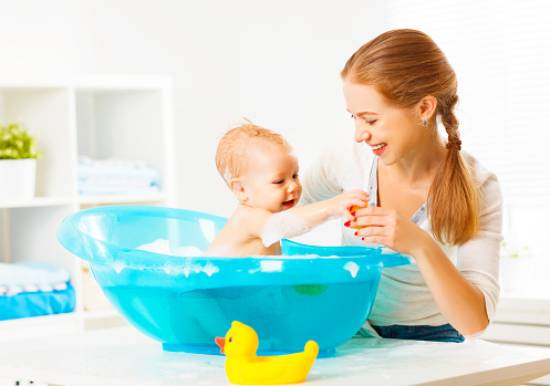 Happy family mother bathes the baby in a blue bath