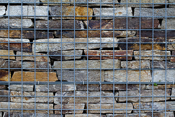 wand aus flusssteinen, die von metallischem netz getragen werden - wall covering decor wall surrounding wall stock-fotos und bilder