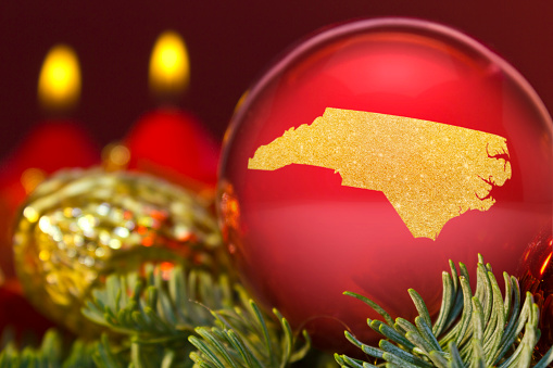 A glossy red bauble with the golden shape of North Carolina.(series)