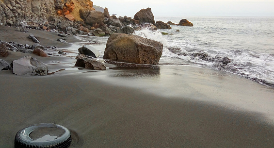Waves roll in on a corner beach filled with rocks and abandoned tire