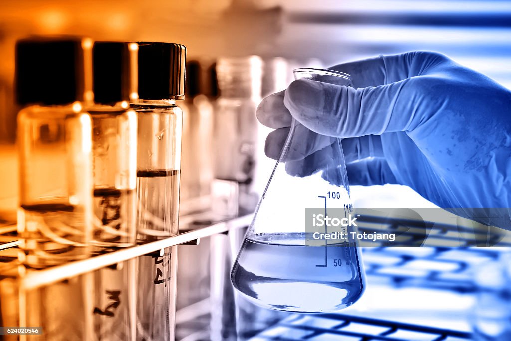 Flask in scientist hand Flask in scientist hand with test tubes in laboratory Analyzing Stock Photo