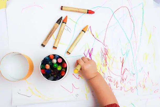 Photo of Baby's hand drawing on the white paper with colorful crayons