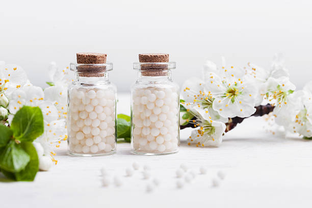 pilules homéopathiques avec des fleurs de printemps sur fond de bois blanc - homeopath photos et images de collection