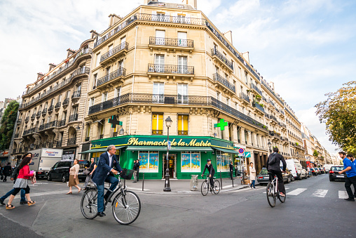 Paris, France - September 26, 2016: People cycling in Paris, France. Pharmacy on background. 