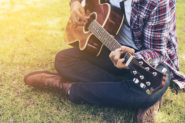 istock Man 's hand playing guitar, sitting on green grass 624056524