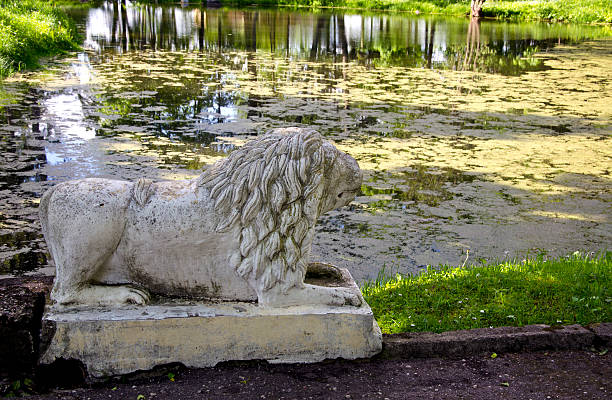 istock Ancient lion sculpture near old pond in park 624086426