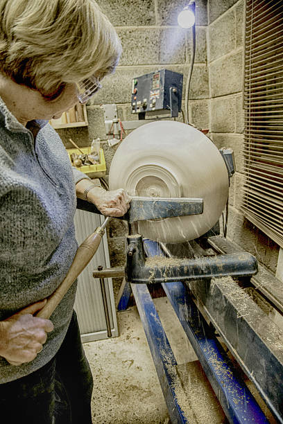 senior woman using chisel and lathe to create wooden bowl