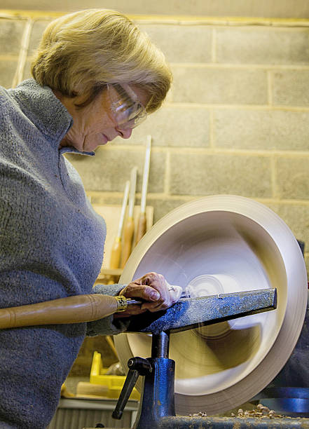 senior woman using chisel and lathe to create wooden bowl