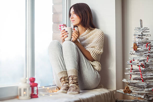 istock Happy beautiful woman drinking hot coffee sitting on window sill 624107864