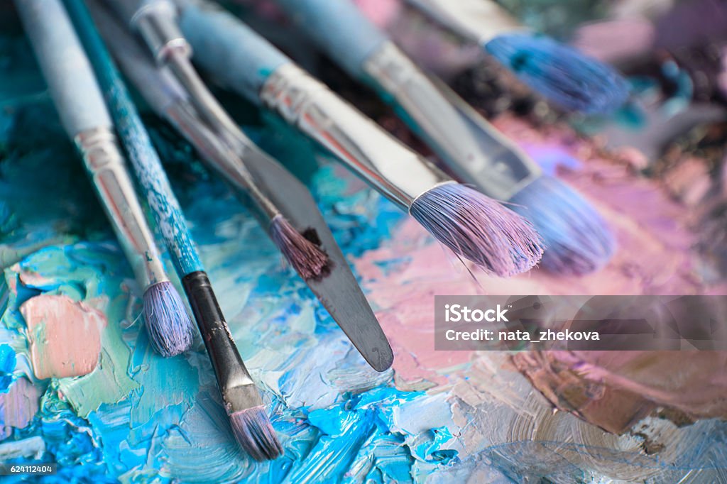 macro artist's palette, texture mixed oil paints in different co artists brushes and oil paints on wooden palette. macro artist's palette, texture mixed oil paints in different colors and saturation. palette with paintbrush and palette-knife. Brushes on canvas Painting - Activity Stock Photo