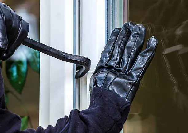A burglar opens a window with a breaker. He wears gloves and lifts the window.