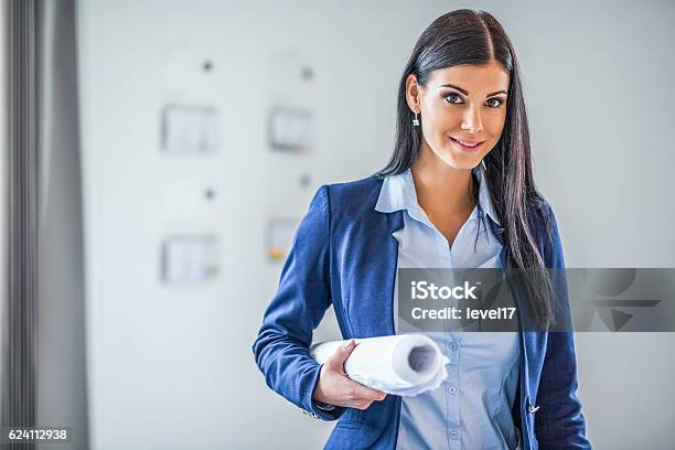 Portrait Of Confident Young Businesswoman Holding Blueprint In Office Stock Photo - Download Image Now