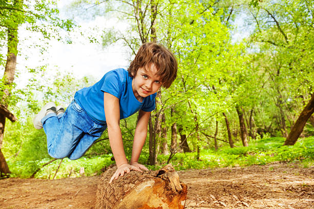 Close-up portrait of young boy jumping over the log in the forest