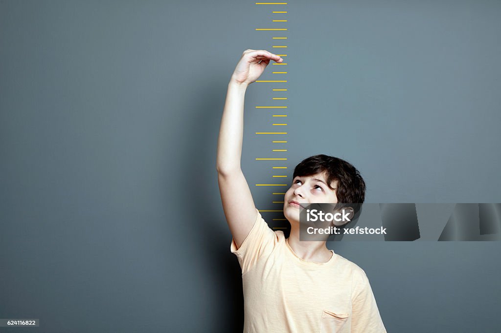 Menino bonito está mostrando altura em uma escala de parede - Foto de stock de Altura Humana royalty-free