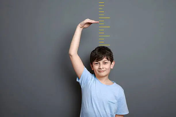 A cute boy is holding his arm up and showing his height on a wall scale.A cute boy is holding his arm up and showing his height on a wall scale.