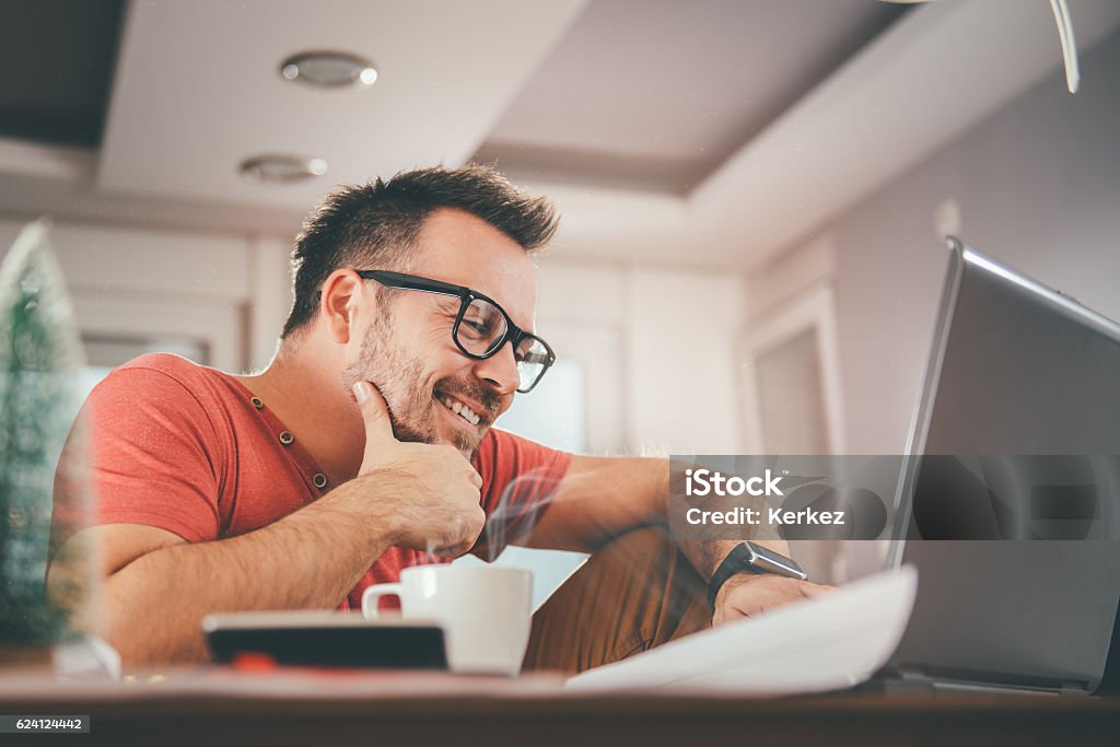 Man working on laptop Man in red shirt smiling and using laptop at office Red Stock Photo