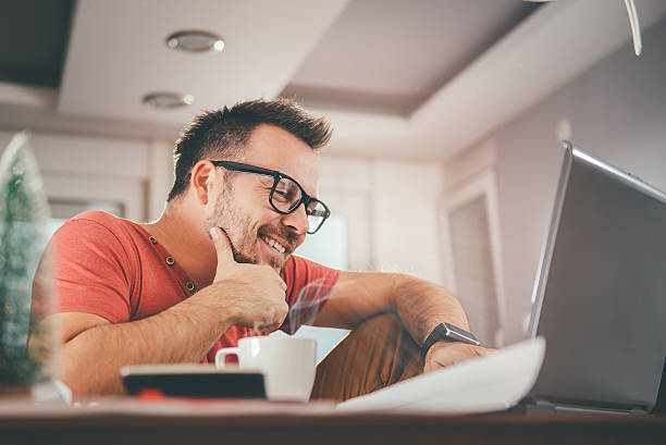 Man working on laptop Man in red shirt smiling and using laptop at office smart watch business stock pictures, royalty-free photos & images