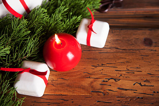 Close-up view of a red Christmas candle on wooden table with cedar tree branch, red ribbons, and white gifts.   NOTE:  This image created for the Getty Creative Content Brief #663372617.