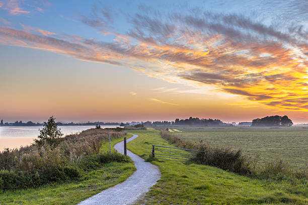 Holland landscape with winding cycling track Holland Polder landscape with winding cycling track along river under beautiful sunset flood plain photos stock pictures, royalty-free photos & images
