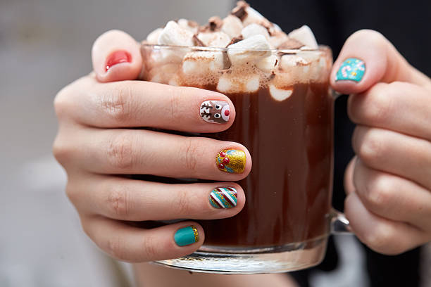 Mug with cocoa and marshmallows in female hands. Female hands with bright festive manicure design holding glass mug with hot cocoa and marshmallows. Winter holidays. Christmas and New Year. chocolate fingers stock pictures, royalty-free photos & images