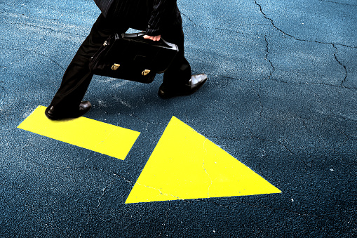 close up elevated view of businessman walking on street with directional sign of yellow arrow
