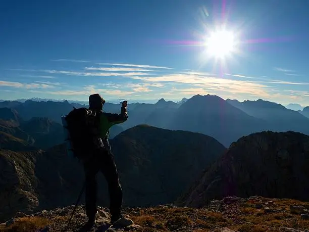 Photo of Hiker takes phone photo. Man photograph on Alps mountain peak.