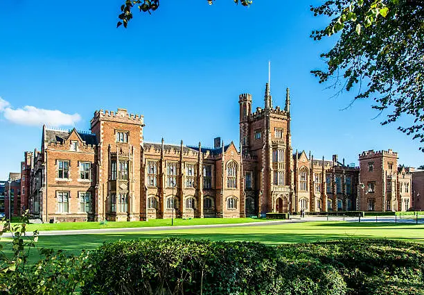 The Queen's University of Belfast with a grass lawn, tree branches and a hedge in sunset light